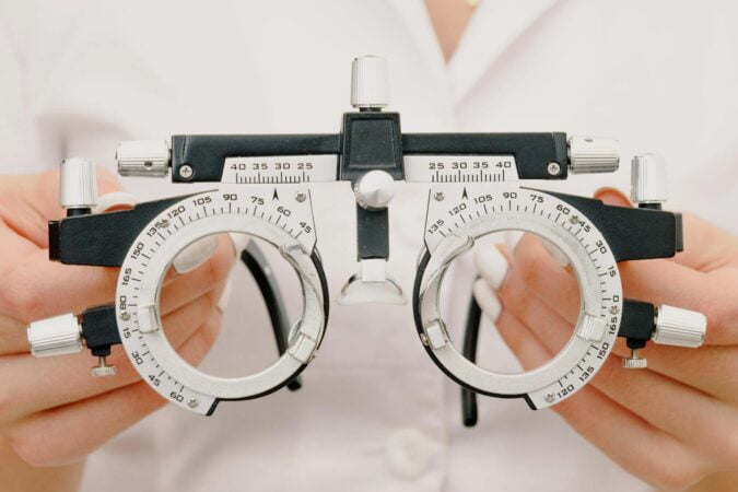 Crop anonymous female optometrist wearing medical robe holding modern trial frame with lenses in hands in modern optometry clinic